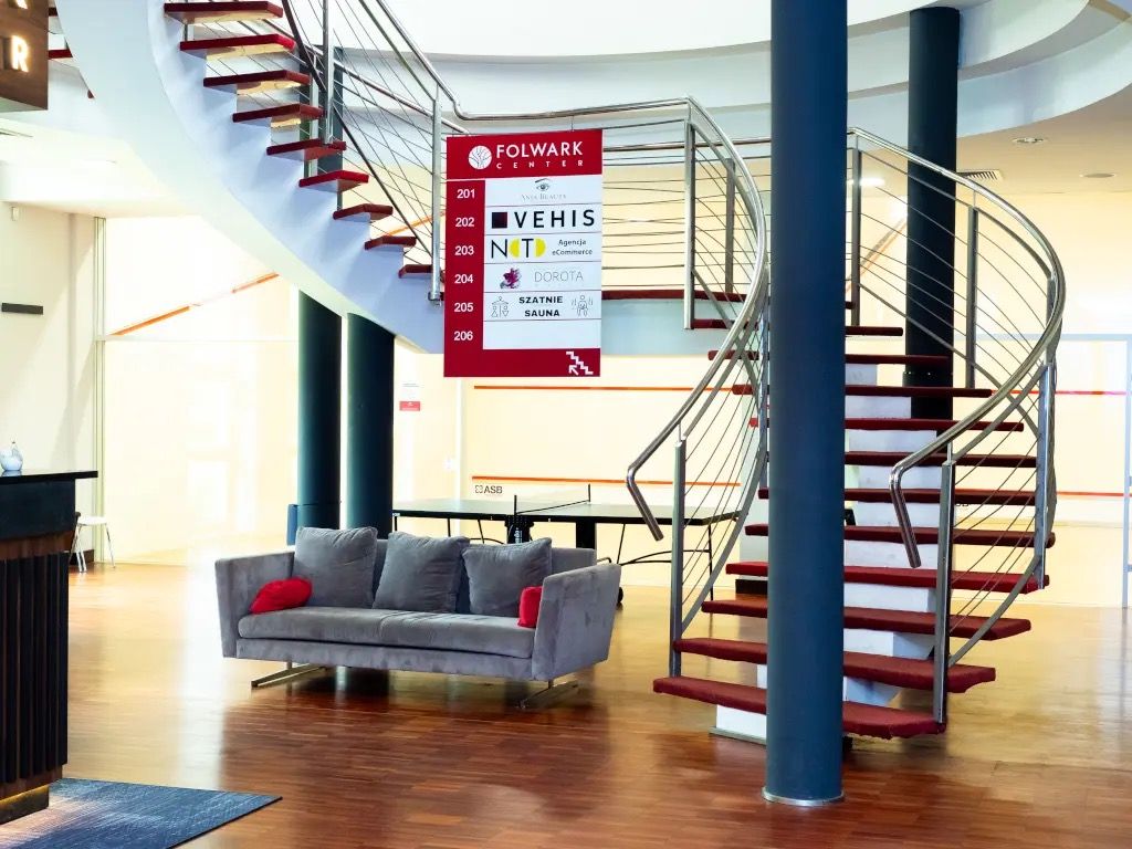 Strefa wspólna klubu Folwark Center ze spiralnymi schodami, kanapą i stołem do tenisa stołowego